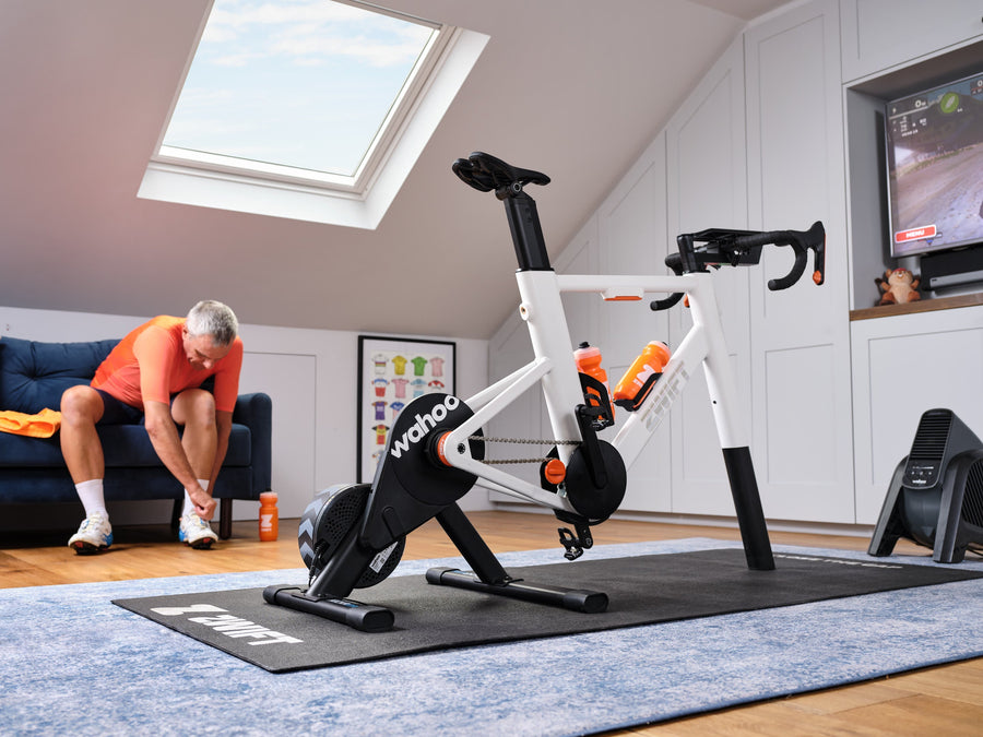 Cycliste qui s'installe sur un vélo d'entraînement Zwift Ride monté sur une base Wahoo, dans une pièce mansardée