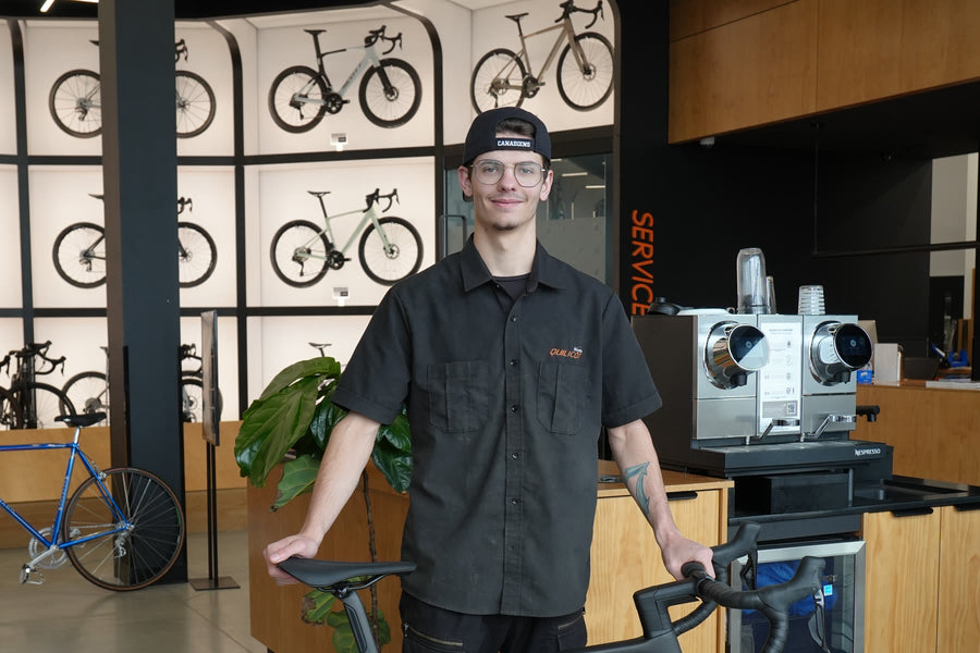 Niki, technicien chez Bicycles Quilicot à Mascouche, casquette des Canadiens à l'envers, les mains sur un vélo de route devant le mur de vélos de la boutique
