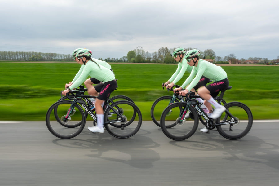 Quatre cyclistes en maillot vert pâle roulent deux par deux sur des vélos de route Van Rysel, vues de profil, dans la campagne